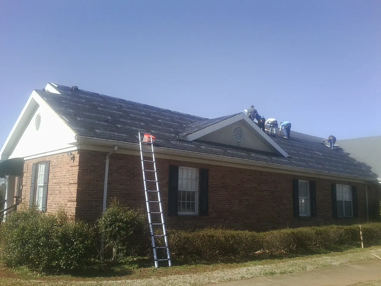Crew tearing shingles off a brick ranch roof with a ladder set — Metal Roof Repair work by our crew in Kenvil