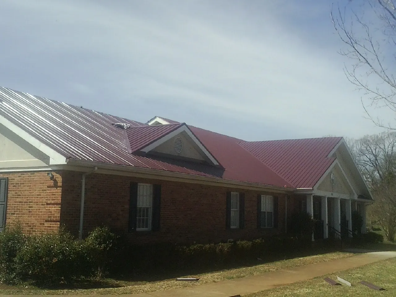 Red metal roof with gabled entries on a long brick building, from a Hail Damage Roof Repair job in Kenvil
