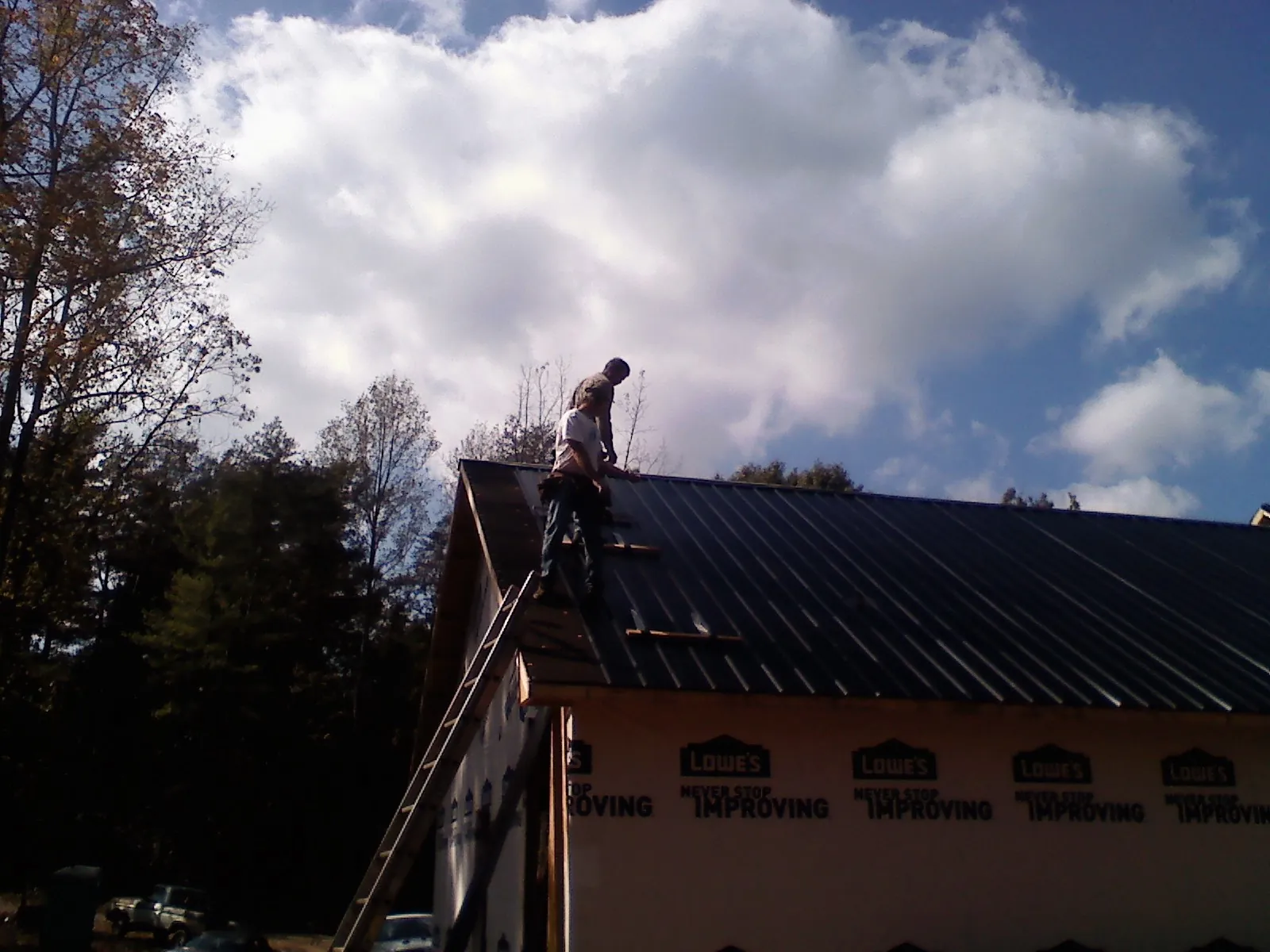 Roofer fastening dark metal panels high against a cloudy sky, from a Roof Inspection job in Kenvil
