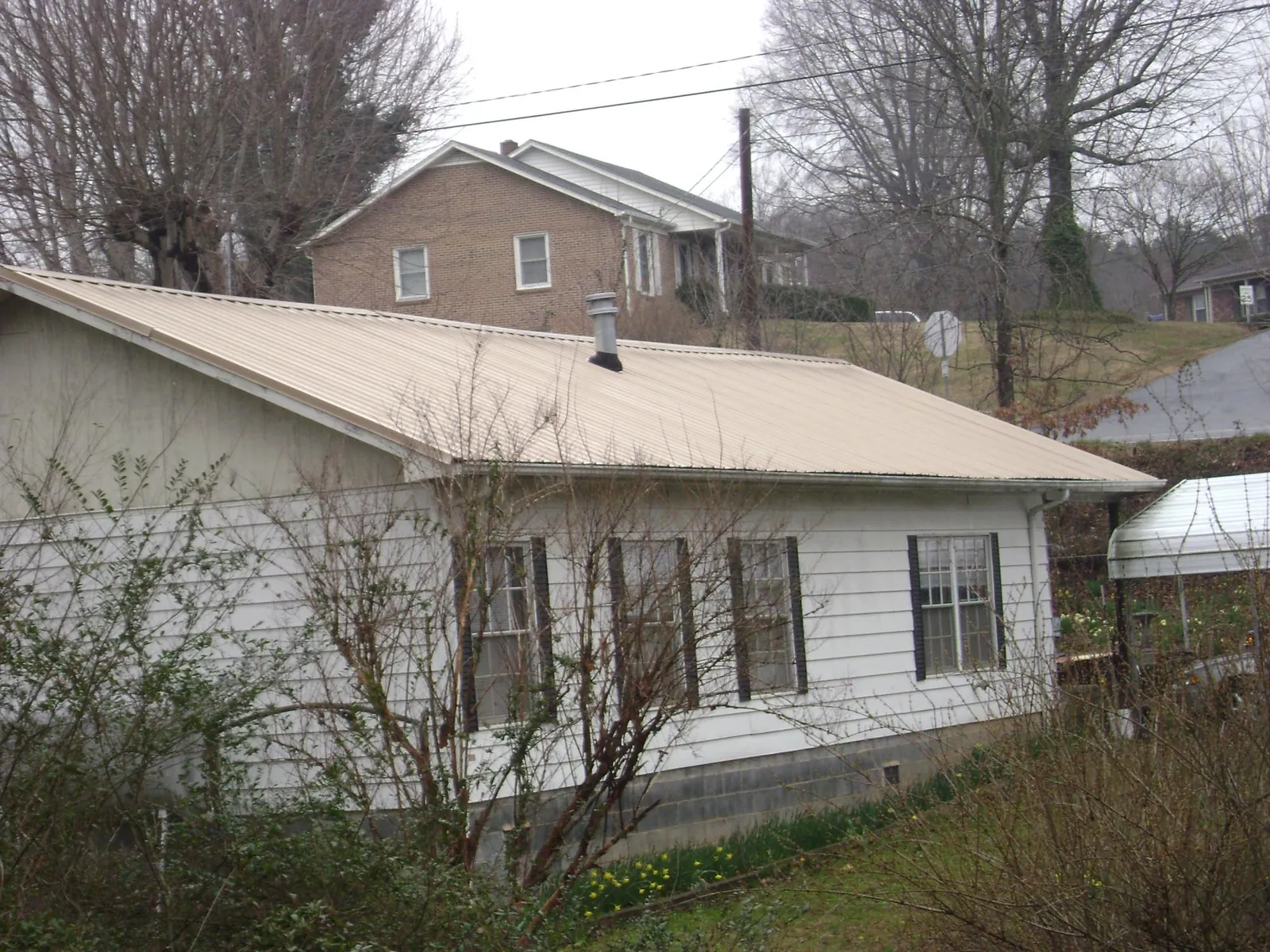 Tan metal roof on a white sided house set into a hillside — Commercial Roofing by Roofing Brothers in Kenvil